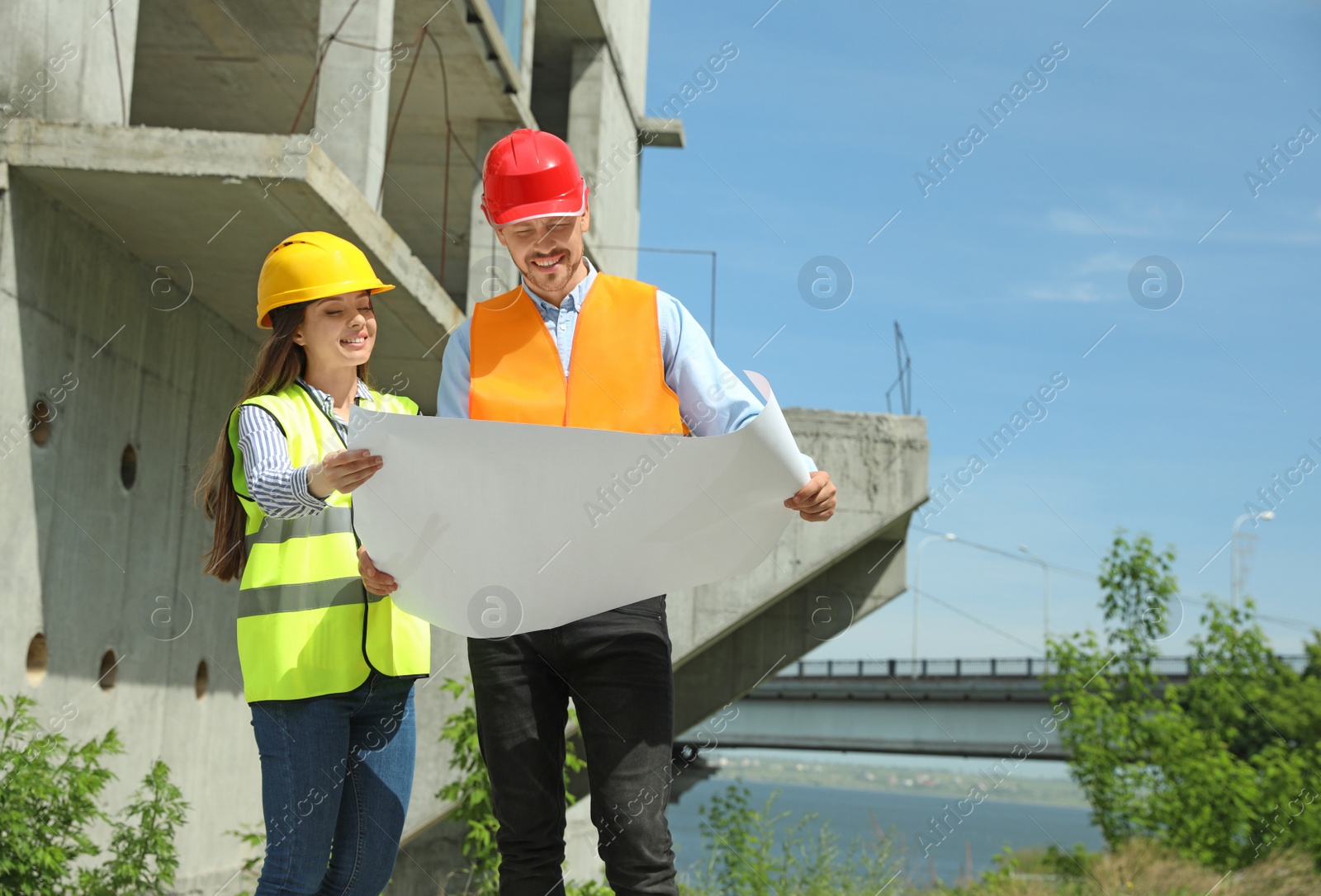 Photo of Professional engineers in safety equipment with drafting at construction site. Space for text