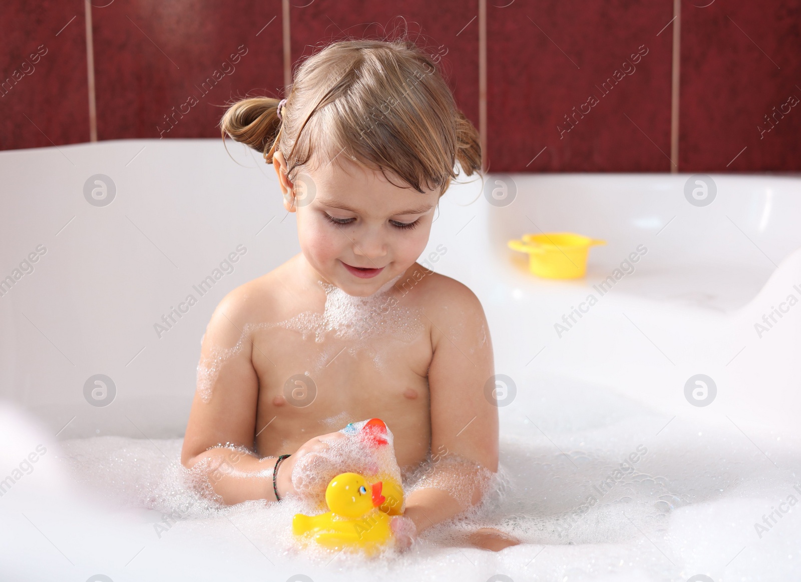 Photo of Little girl bathing with toy ducks in tub