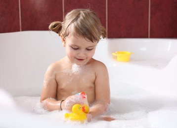 Photo of Little girl bathing with toy ducks in tub