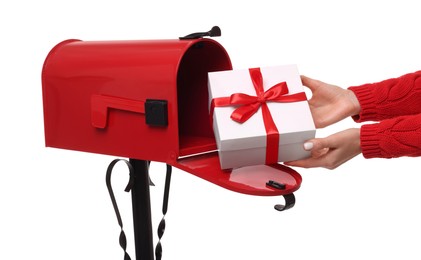 Woman putting Christmas gift into mailbox on white background, closeup. Sending present by mail