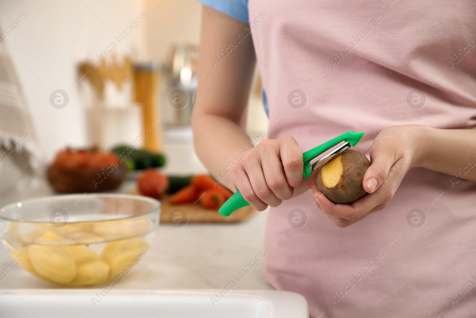 Photo of Woman peeling potato in kitchen, closeup. Preparing vegetable