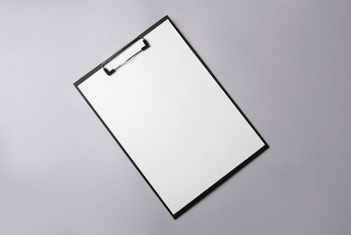 Photo of Black clipboard with sheet of blank paper on light grey background, top view