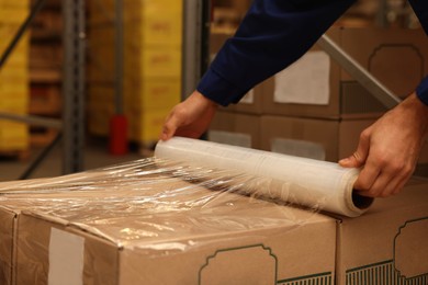 Worker wrapping boxes in stretch film at warehouse, closeup