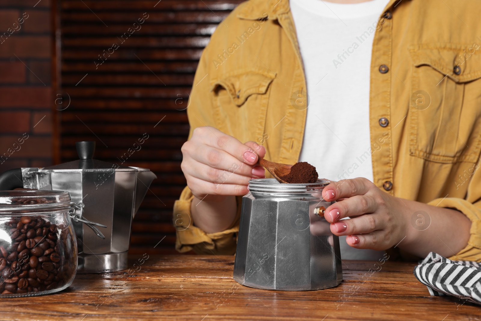 Photo of Woman putting ground coffee into moka pot at wooden table, closeup