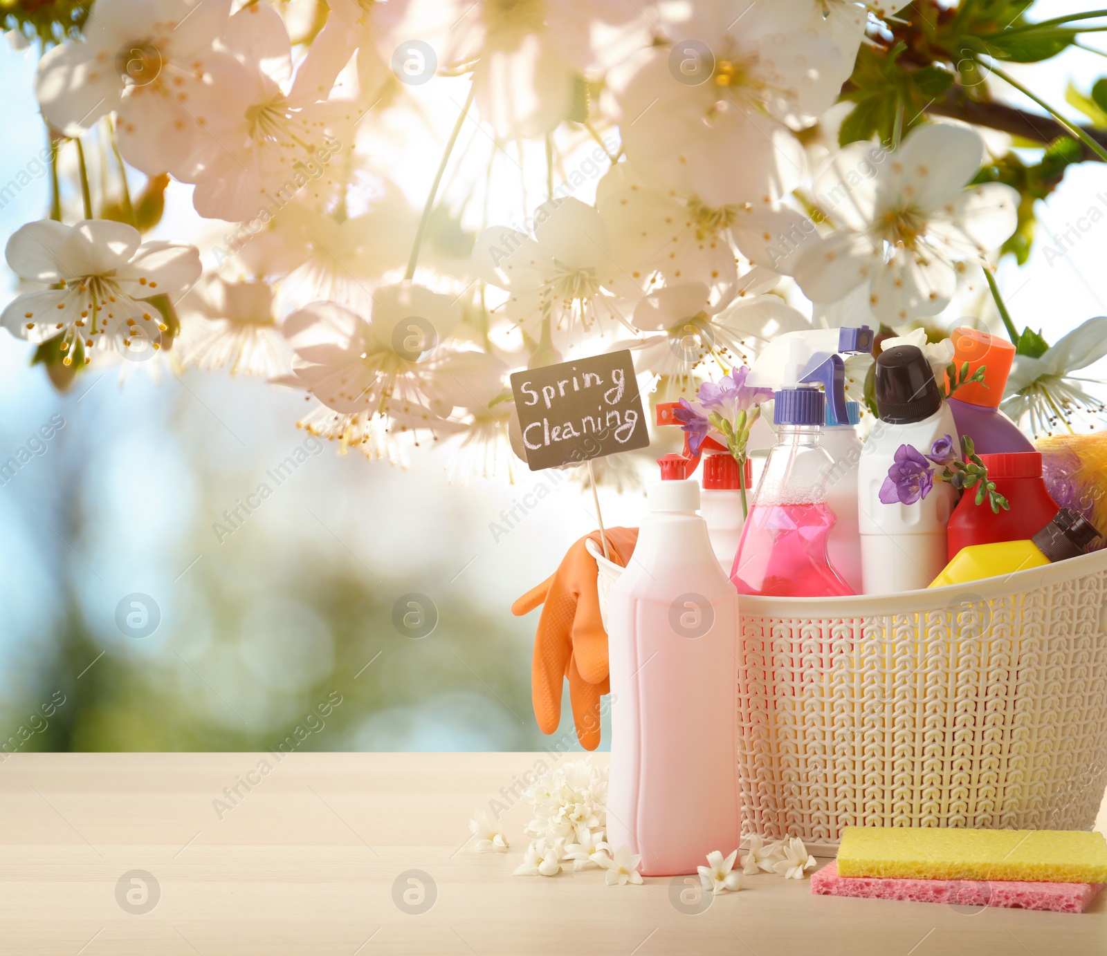 Image of Plastic basket with different detergents on wooden table, space for text. Spring cleaning concept 