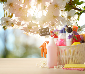 Image of Plastic basket with different detergents on wooden table, space for text. Spring cleaning concept 