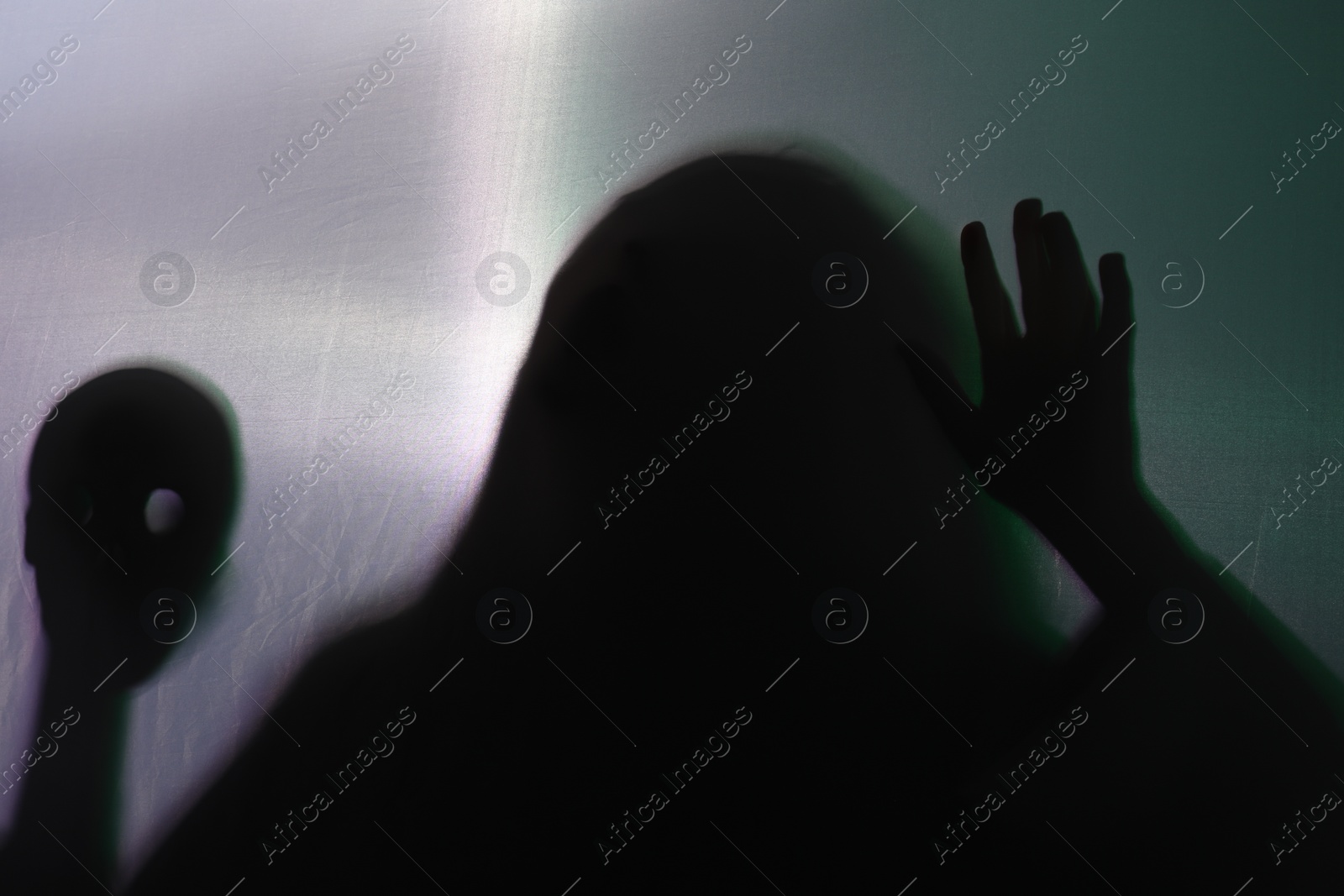 Photo of Silhouette of creepy ghost with skull behind cloth against grey background