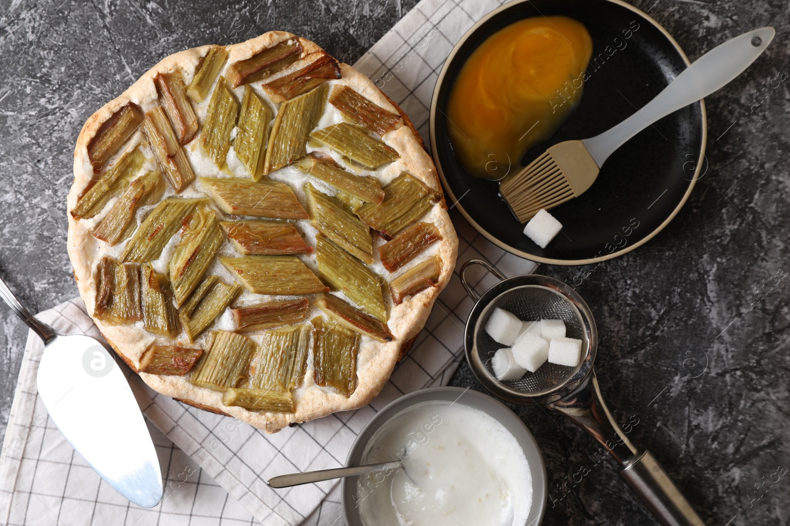 Photo of Freshly baked rhubarb pie and ingredients on grey textured table, flat lay