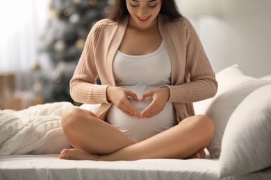 Photo of Happy pregnant woman on bed in room decorated for Christmas, closeup. Expecting baby