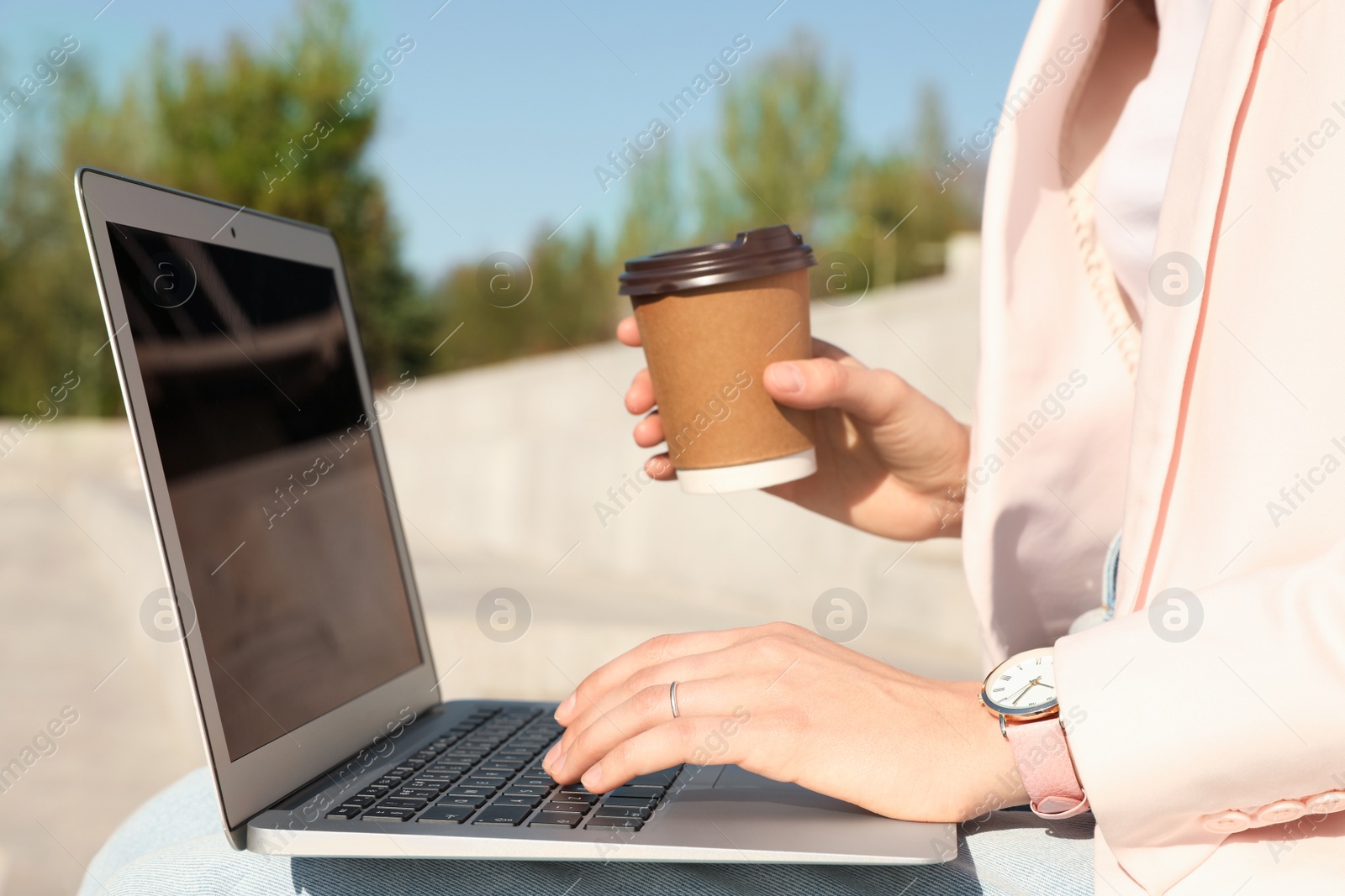 Image of Young woman with coffee working on laptop outdoors, closeup