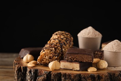 Photo of Different tasty energy bars, nuts and protein powder on wooden stump, closeup