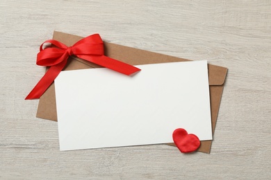 Blank card, envelope and decorative heart on wooden background, flat lay with space for text. Valentine's Day celebration