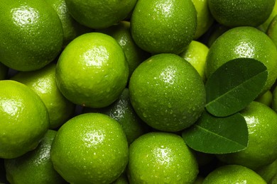 Photo of Fresh ripe limes and leaves with water drops as background, top view