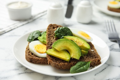 Photo of Tasty avocado toasts with quail egg on white marble table