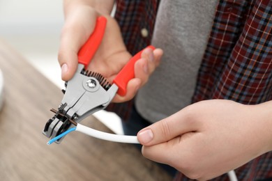 Photo of Professional electrician stripping wiring at wooden table, closeup