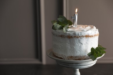 Photo of Tasty Birthday cake with burning candle and eucalyptus branches on grey table, closeup. Space for text