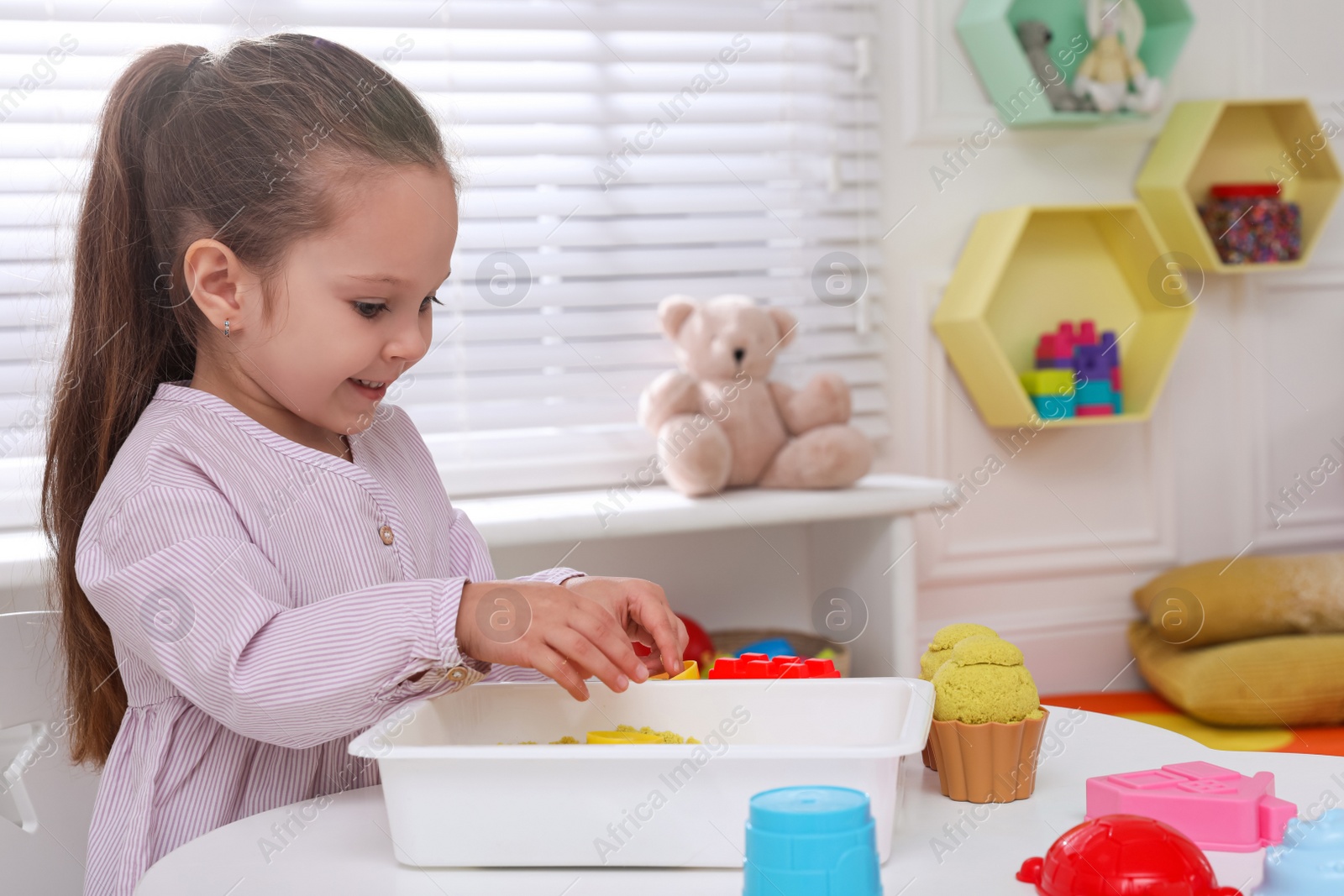 Photo of Cute little girl playing with bright kinetic sand at table in room