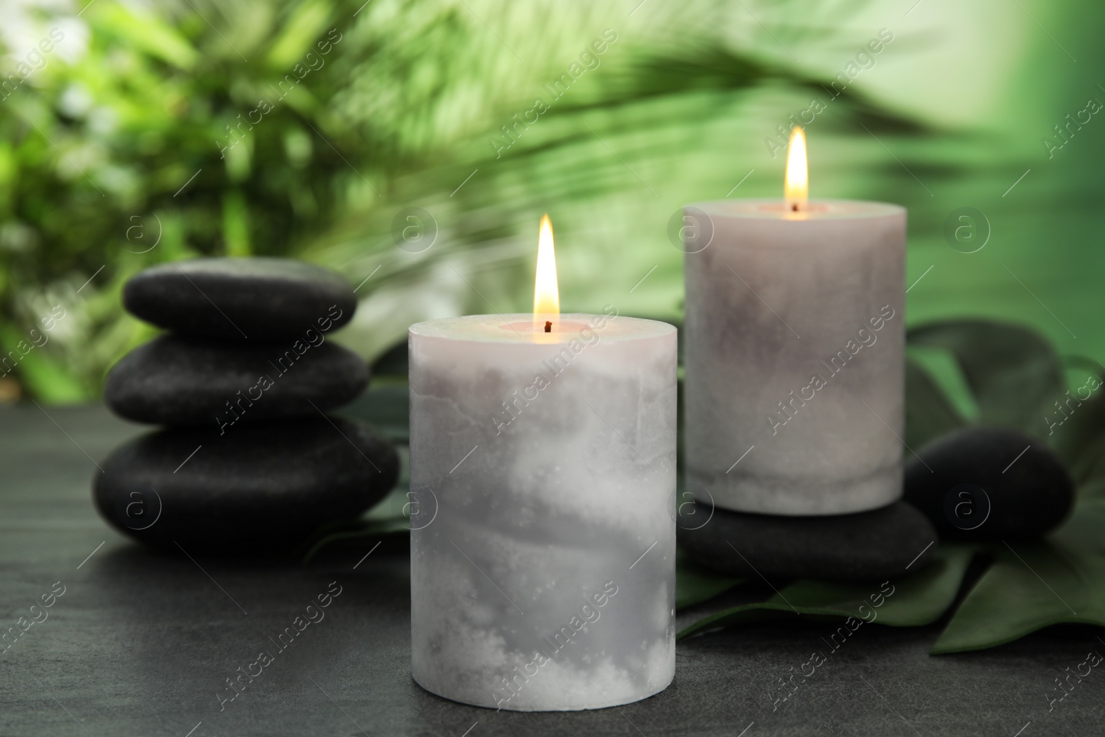 Photo of Burning candles and spa stones on grey table against blurred green background