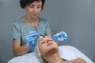 Photo of Cosmetologist applying cosmetic product for chemical peeling on client's face in salon