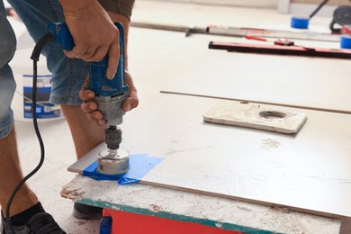 Photo of Worker making socket hole in tile indoors, closeup