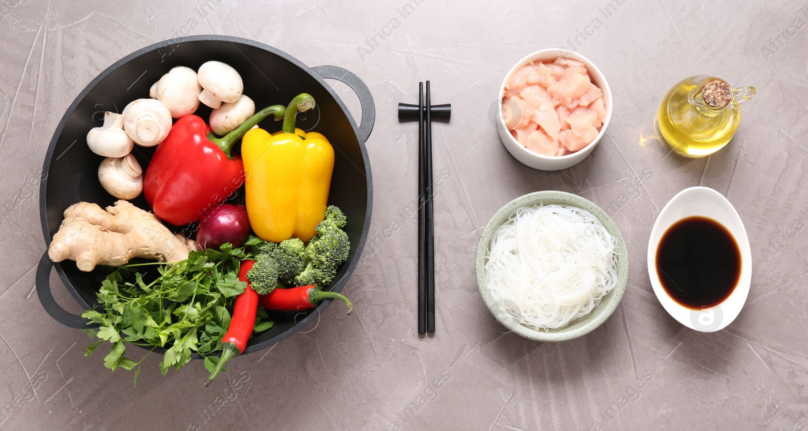 Photo of Wok, chopsticks and different products on grey textured table, flat lay