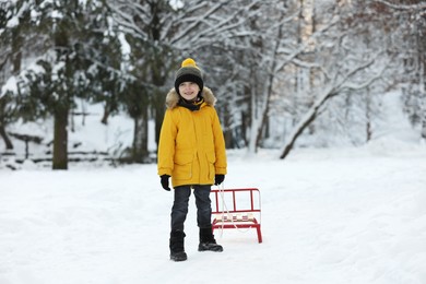 Photo of Little boy pulling sledge through snow in winter park