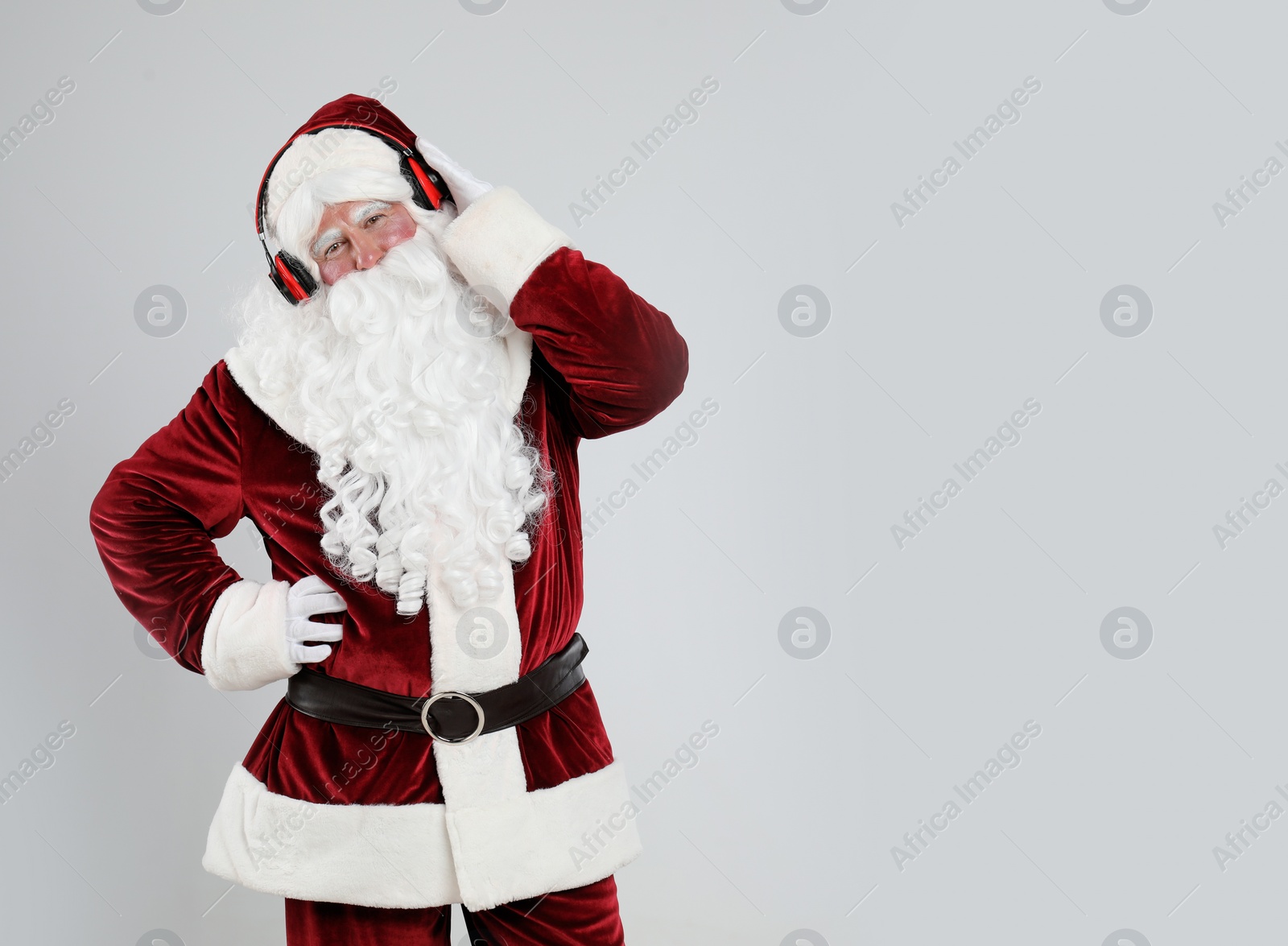 Photo of Santa Claus with headphones listening to Christmas music on light grey background. Space for text