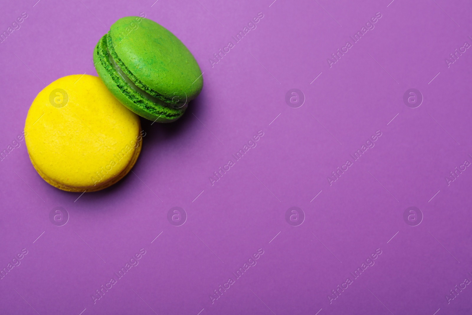 Photo of Delicious colorful macarons on purple background, flat lay. Space for text
