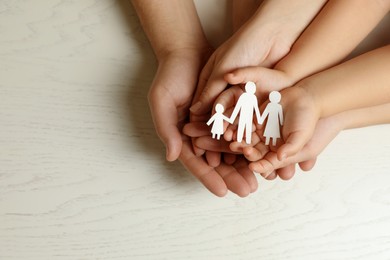 Parents and child holding paper cutout of family at white wooden table, top view