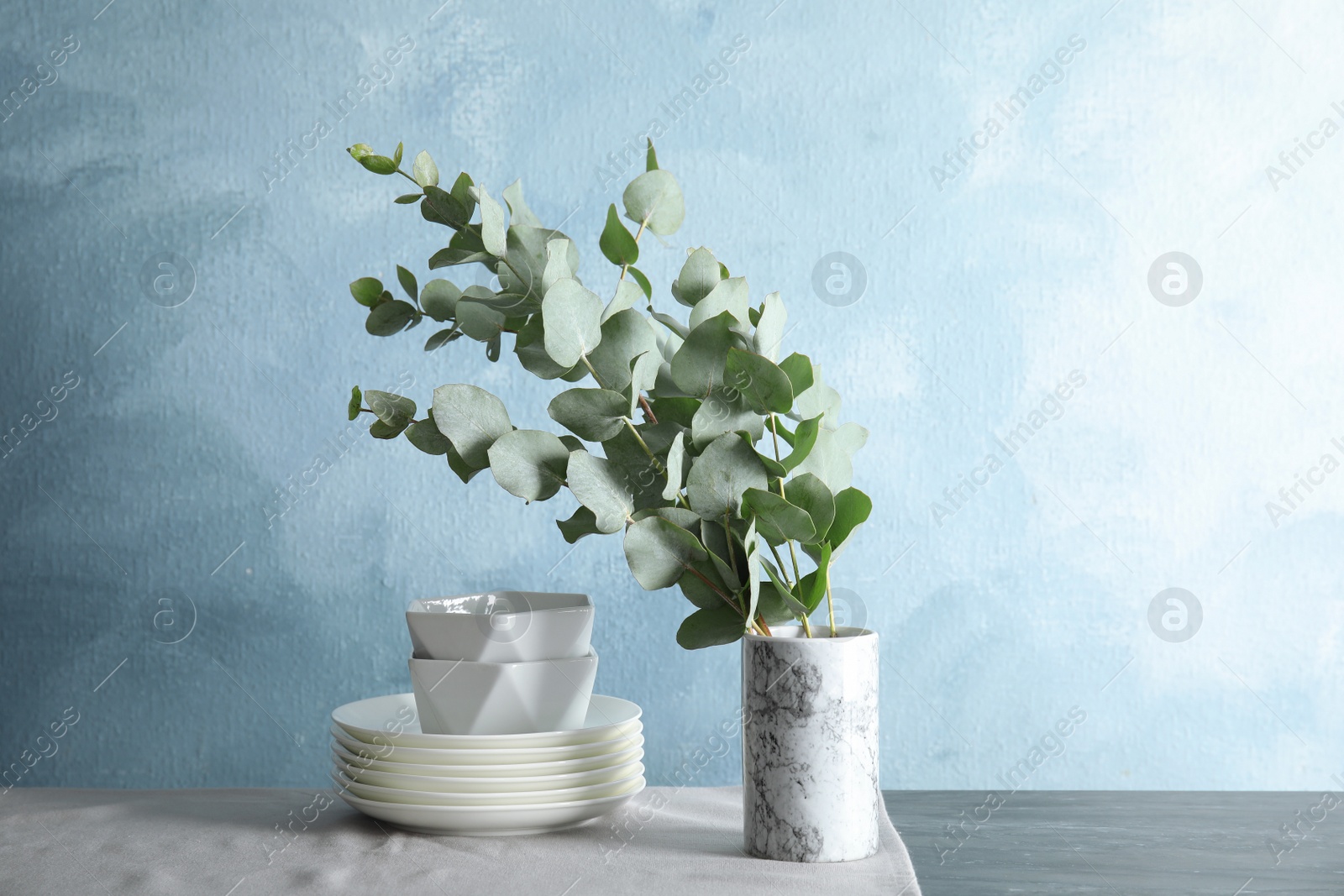 Photo of Bunch of eucalyptus branches with fresh leaves in vase and dishware on table