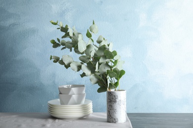 Bunch of eucalyptus branches with fresh leaves in vase and dishware on table