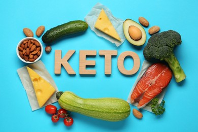 Photo of Word Keto of wooden letters and different products on light blue background, flat lay