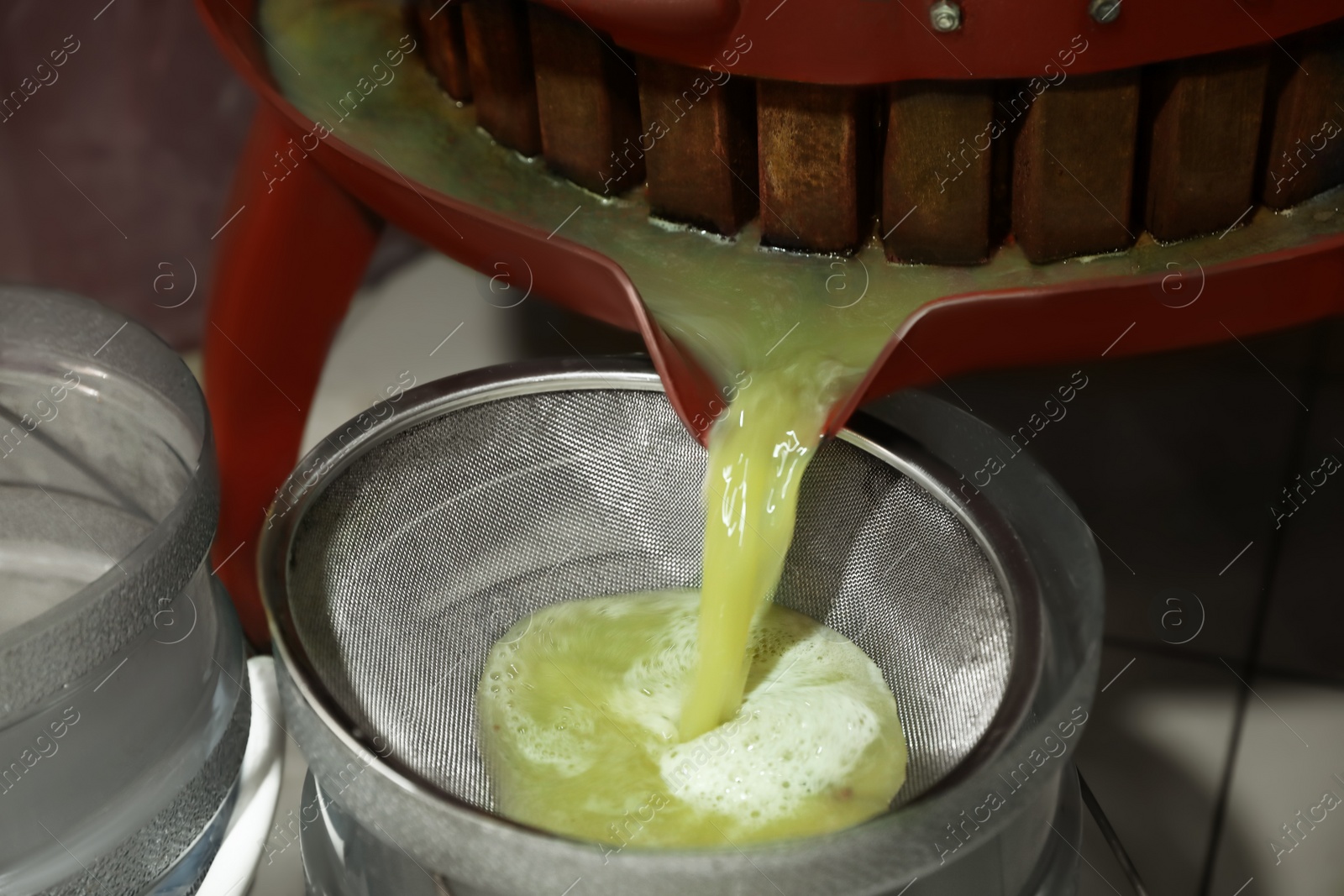 Photo of Grape juice pouring from wooden wine press into bucket indoors, closeup