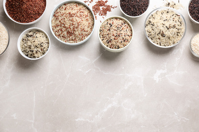 Photo of Different sorts of rice on light grey marble table, flat lay. Space for text