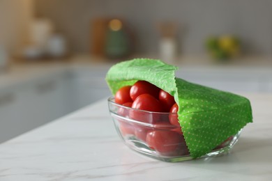 Photo of Tomatoes in bowl covered with beeswax food wrap on white table indoors, closeup. Space for text