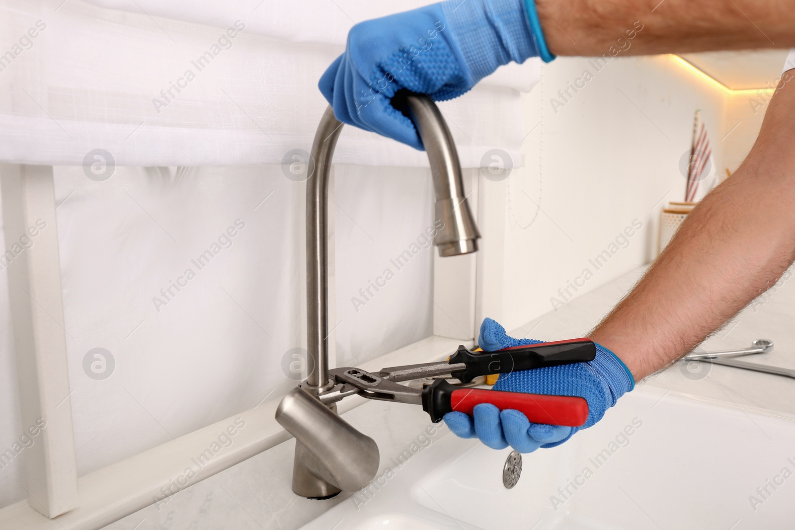 Photo of Man repairing water tap with wrench in kitchen, closeup