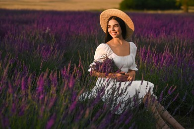 Photo of Beautiful young woman with bouquet sitting in lavender field at sunset