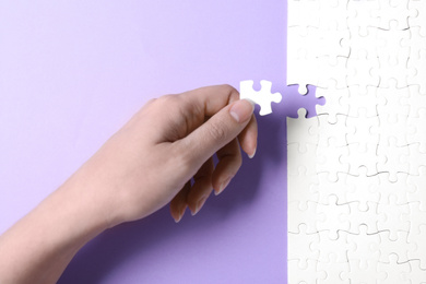 Photo of Woman putting last piece of white puzzle on violet background, closeup