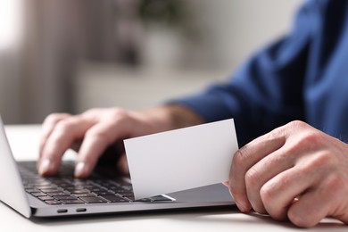 Photo of Man with laptop holding blank business card at white table indoors, closeup