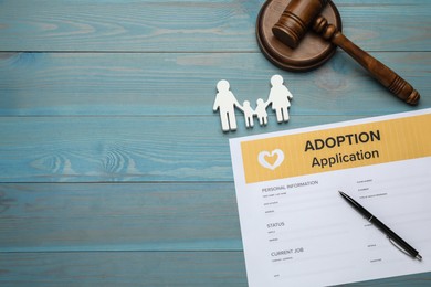 Photo of Adoption application, gavel, family figure and pen on blue wooden table, flat lay. Space for text