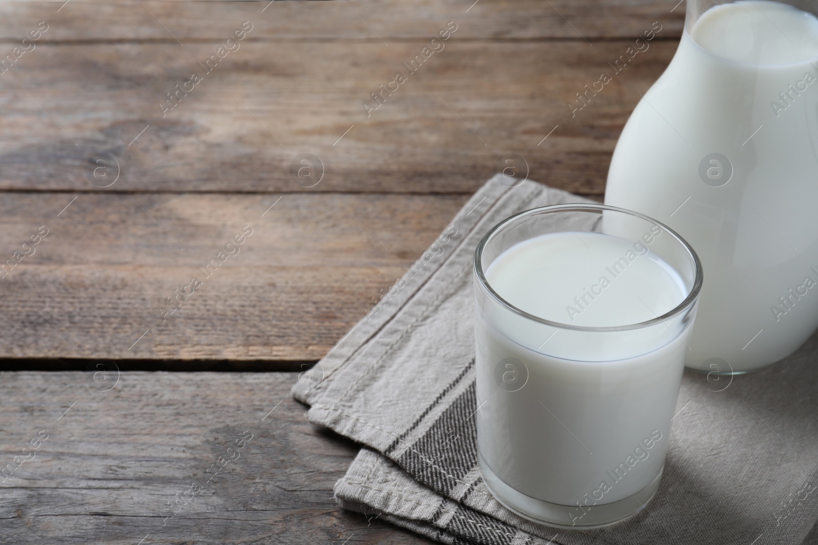 Photo of Glass and jug with fresh milk on wooden table. Space for text