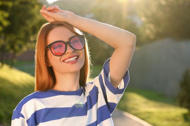 Beautiful smiling woman wearing sunglasses in park, space for text