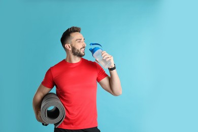 Photo of Handsome man with yoga mat drinking water on turquoise background. Space for text