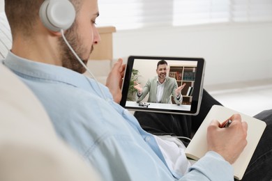 Image of Young man with headphones and modern tablet at online lesson. E-learning