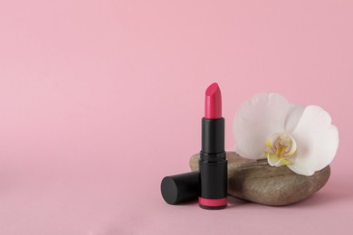 Photo of Beautiful lipstick on stone and orchid flower against pink background, space for text