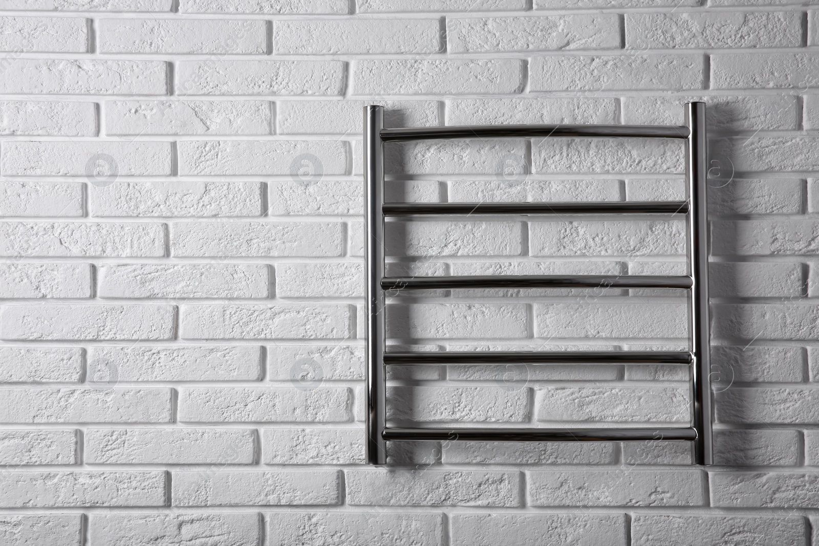 Photo of Modern heated towel rail on white brick wall. Space for text