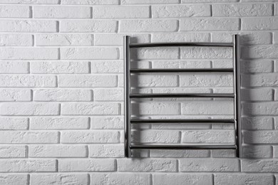 Modern heated towel rail on white brick wall. Space for text