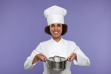 Photo of Happy female chef in uniform holding cooking pot on purple background