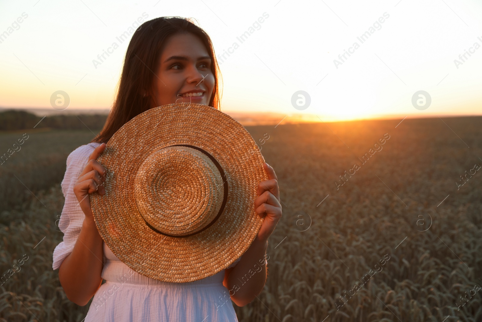 Photo of Beautiful young woman with straw hat in ripe wheat field at sunset, space for text