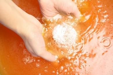 Photo of Woman holding bath bomb in orange water, closeup